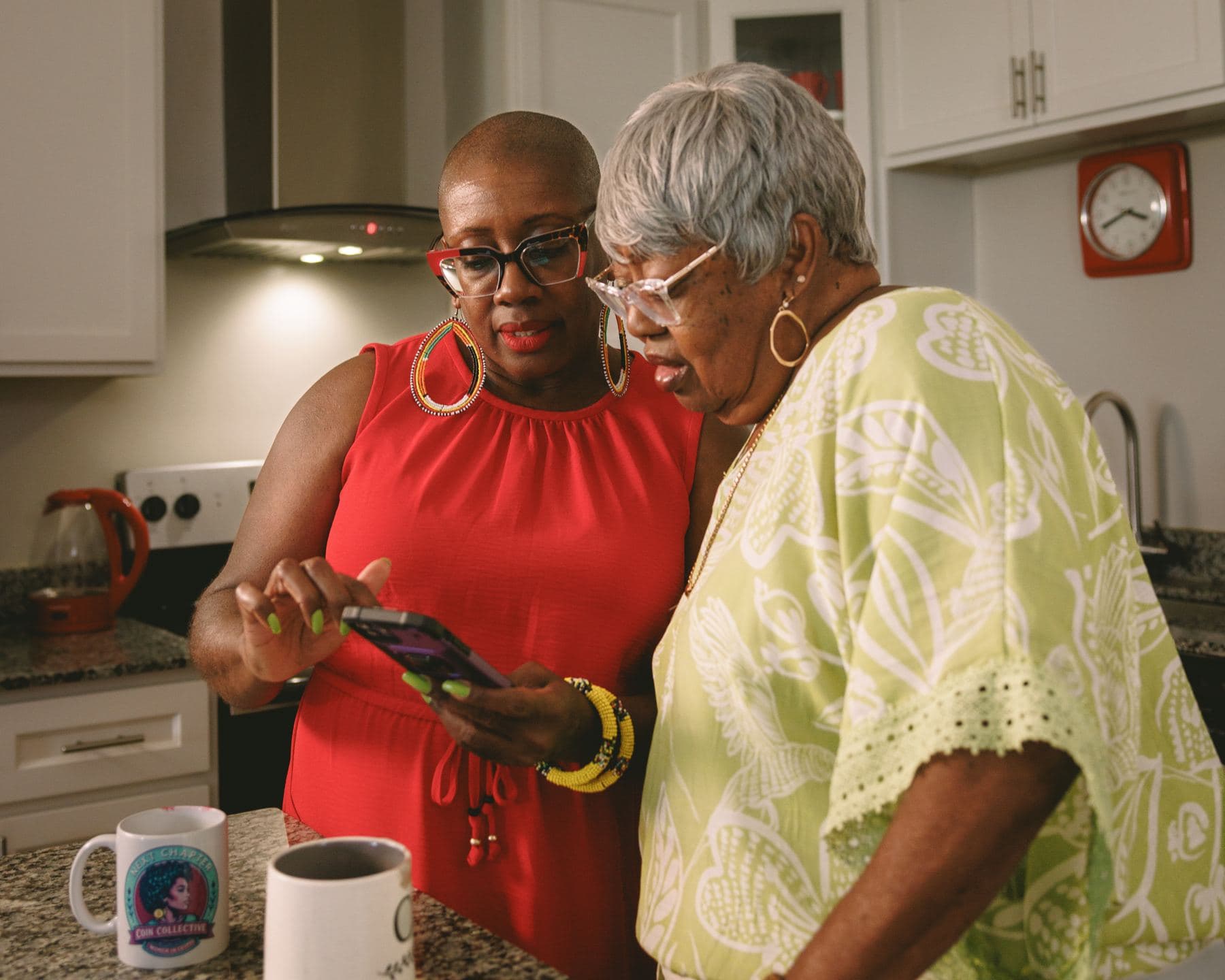 A woman showing her mother something on her phone in their kitchen