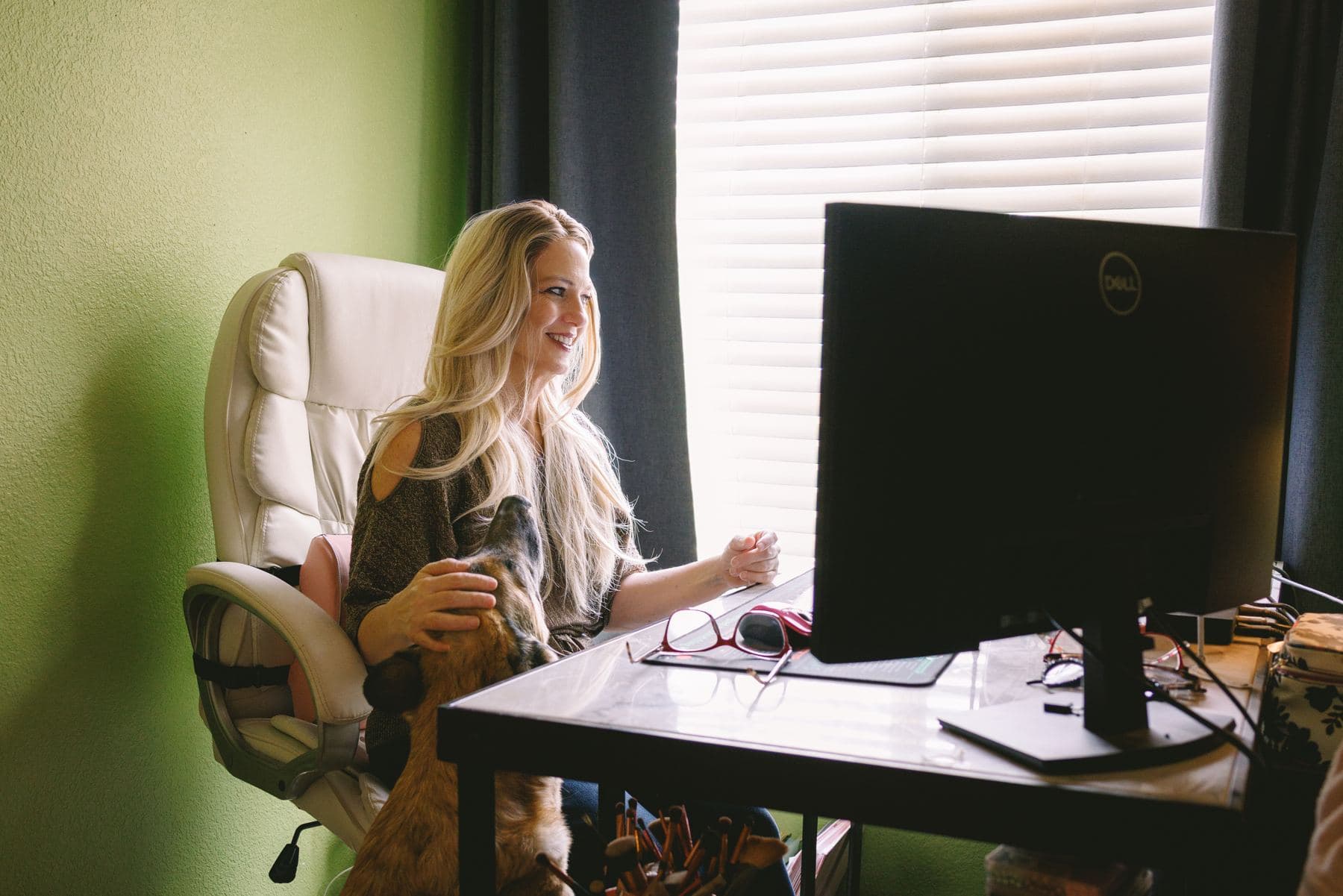 A woman smiling at her computer with her dog on her lap