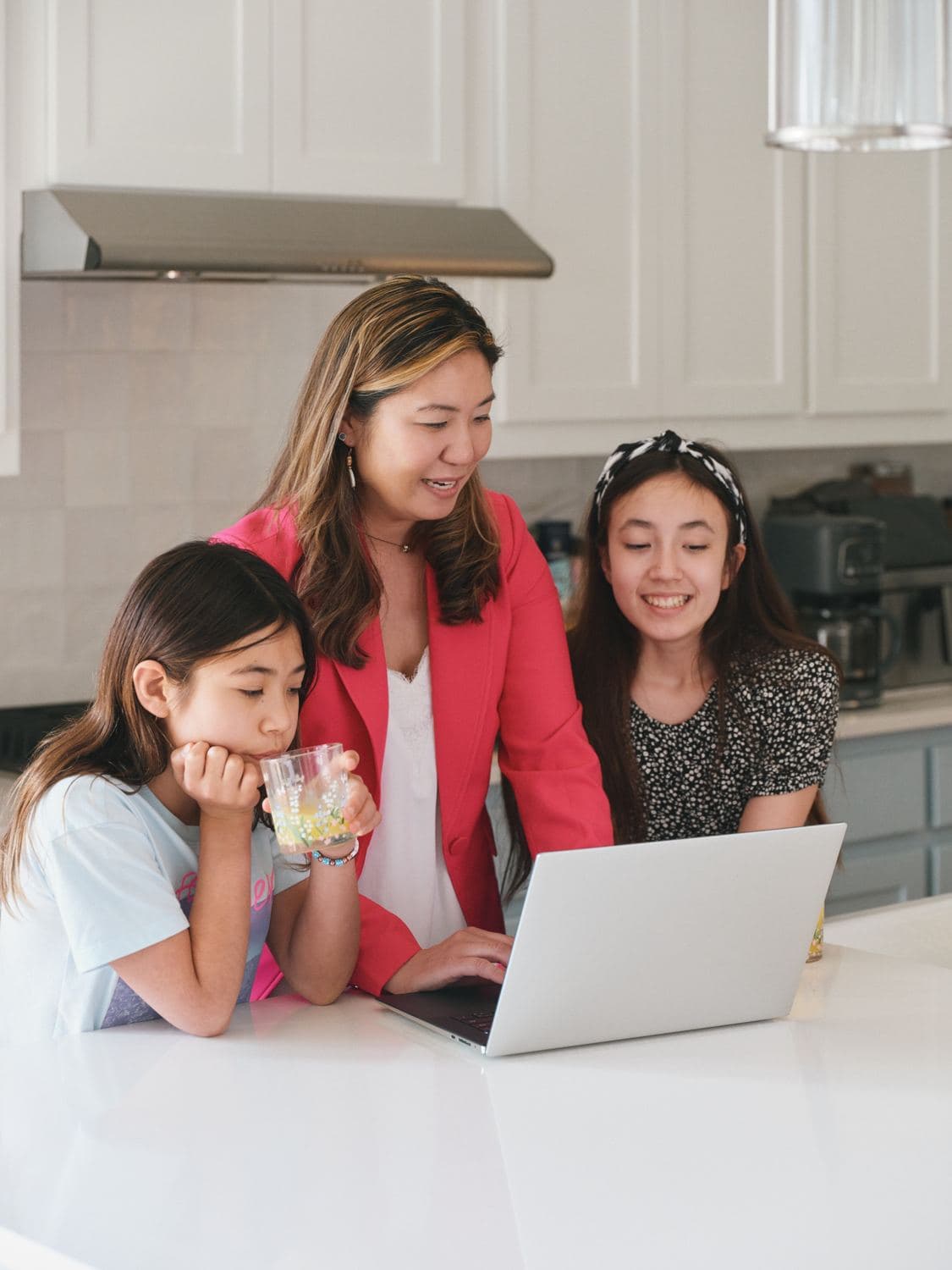A mother and her two daughters looking at a laptop together in their kitchen